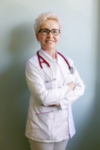 Zdjęcie dr Krystyny Komnaty, w białym stroju lekarskim, ze stetoskopem na szyi.