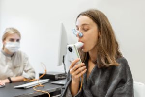 Zdjęcie kobiety wykonującej spirometrię, w tle lekarz przy komputerze
